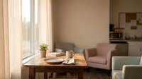 Cozy modern living room interior with wooden dining table, coffee cup, plant and comfortable seating in warm natural lighting for home decor.