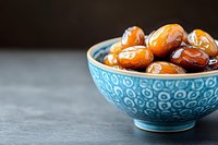Fresh sweet dates in traditional blue ceramic bowl on dark background, healthy dried fruit snack for natural energy boost and nutrition.