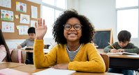 Happy African American elementary school girl raising hand in classroom with yellow cardigan and glasses, eager to participate in lesson.