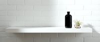 Minimalist white shelf against brick wall displaying black bottle and small potted plant, clean modern interior design aesthetic for home decor.