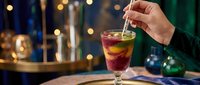 Person holding a glass of cola with ice and straw at an elegant bar setting with blurred bokeh lights and bottles in background for beverage, hospitality, nightlife, and cocktail concepts.