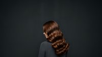 Brunette woman with long wavy hair styled in vintage waves, shown in profile against dark background. Suitable for hair care, beauty, and salon marketing materials.