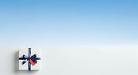 White gift box with navy blue ribbon bow and red accent on light blue background, suitable for holiday greeting cards, promotional materials, and seasonal marketing campaigns.
