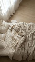 Unmade bed with beige linen bedding, open books, and white sheer curtains in bright natural light, suitable for lifestyle and home decor content.