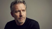 Mature Caucasian businessman with gray beard in black sweater looking thoughtful against neutral background for corporate marketing materials.