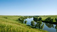 River winding through lush green meadows and grasslands under clear blue sky, suitable for nature, landscape, and environmental design projects.