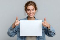 Young Caucasian woman in denim jacket holding blank white sign with thumbs up gesture against gray background. Positive expression for advertising mockup.