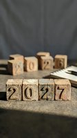 Wooden blocks displaying 2027 in foreground with blurred 2026 blocks behind, symbolizing year transition and future planning on rustic surface.