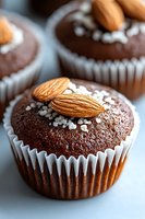 Chocolate muffins topped with whole almonds and sugar crystals in white paper cups, macro food photography with selective focus and natural lighting.