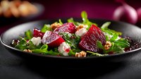 Fresh beet and arugula salad with crumbled feta cheese, walnuts and olive oil dressing served on black ceramic plate against dark background.
