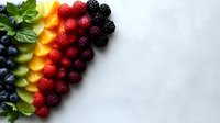 Fresh colorful berries and fruits arranged in rainbow pattern with mint leaves on light gray background, healthy eating concept for food design and menu.