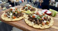 Authentic Mexican street tacos with seasoned ground meat, fresh cilantro, diced onions, tomatoes and lime wedges served on corn tortillas at outdoor food market.