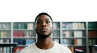 Young Black man wearing casual cream ribbed sweater, looking upward thoughtfully in library setting with bookshelves background. Isolated portrait for education, learning, inspiration, and professional use.