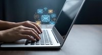 Professional typing on laptop with digital email icons floating above keyboard representing modern communication and messaging technology for business.