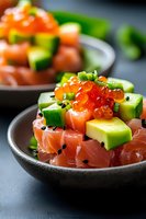 Fresh salmon poke bowl with diced avocado, red caviar, cucumber, green onion and black sesame seeds served in dark ceramic bowl on gray background.
