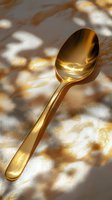 Golden spoon on marble surface with natural shadow overlay creating elegant pattern, luxury dining concept for restaurant and catering business.