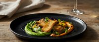 Gourmet seared duck breast with vibrant green pea puree and roasted vegetables elegantly plated on dark ceramic dish for fine dining restaurant menu.