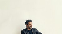 Mature man with dark hair and beard wearing black jacket against neutral beige background, suitable for corporate, business, and professional website design projects.