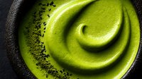 Creamy matcha green tea mousse in dark ceramic bowl with powdered tea garnish, showcasing swirled texture for culinary presentation.