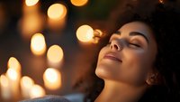 Young woman relaxing with eyes closed in warm ambient lighting with golden bokeh background, expressing serenity and wellness in spa or meditation setting.