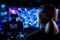 Female photographer capturing bokeh lights at night with professional camera on tripod. Blurred blue and purple city lights create dreamy background atmosphere.