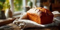 Freshly baked homemade bread loaf on linen cloth by sunny kitchen window. Warm golden lighting creates cozy bakery atmosphere for food blogs and recipes.