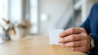 Male professional in business attire holding blank white card for contact information or branding mockup in modern office setting.