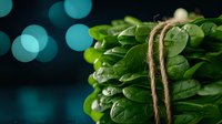 Fresh raw spinach leaves tied with rustic twine on dark background with teal bokeh lights, macro food photography for healthy eating and nutrition concept.