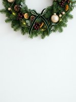 Festive wreath with evergreen branches, gold ornaments, pinecones, berries, and black ribbon bow on white background. Holiday decoration for seasonal greeting cards and winter designs.