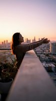 Young woman with arms outstretched embracing freedom on rooftop terrace at sunset with city skyline backdrop for wellness and lifestyle concepts.