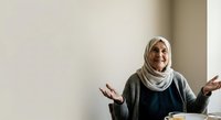 Senior woman wearing hijab gesturing while speaking, expressing communication and discussion in indoor setting.