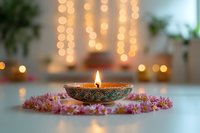 Burning diya lamp surrounded by pink flowers with soft bokeh lights in background creates serene festive atmosphere for meditation and spiritual practices.