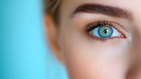 Close up macro shot of bright blue eye with long eyelashes and perfectly shaped eyebrow against turquoise background, showing natural beauty and eye care concept.