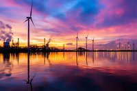 Wind turbines and industrial facility silhouettes against dramatic purple sunset sky, reflecting in calm water surface. Clean energy meets industry concept.