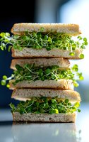 Fresh microgreen sandwich stacked in layers with toasted white bread and vibrant sprouts against dark background, macro food photography for healthy eating concept.