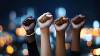 Raised fists of diverse people against blurred city lights background symbolizing unity, solidarity, protest and social justice movement for equality and change.