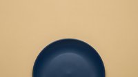 Minimalist dark navy ceramic bowl on neutral beige background, isolated flat lay composition for design, home decor, kitchenware, and tableware projects.
