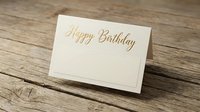 Elegant cream birthday card with gold foil lettering on rustic wooden background for greeting card designs and celebration concepts.