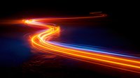 Glowing orange and blue light trails curve along dark background creating dynamic motion effect, suitable for technology and innovation concepts.