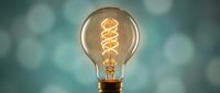 Vintage Edison light bulb with glowing spiral filament against soft bokeh background for creative lighting and electrical concepts.