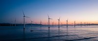 Offshore wind turbines generating renewable energy at sunset with calm ocean waters reflecting purple and orange sky colors creating sustainable power landscape.