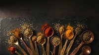 Colorful aromatic spices and herbs in wooden spoons arranged on dark slate background for cooking and seasoning culinary preparations.