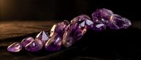 Purple amethyst gemstones scattered on dark wooden surface with warm lighting creating luxury jewelry and crystal healing atmosphere.