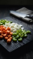 Fresh diced vegetables on dark wooden cutting board with chef knife for healthy cooking and meal preparation in modern kitchen.