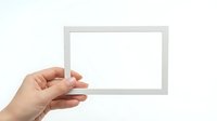 Hand holding blank white picture frame mockup against light background for photo display and artwork presentation.