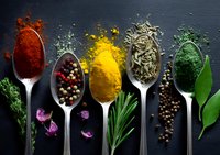 Colorful spices and herbs in silver spoons on dark background - paprika powder, peppercorns, turmeric, dried herbs and spirulina with fresh aromatic ingredients.