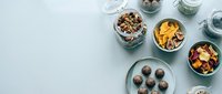 Healthy snack bowls with nuts, dried fruits and energy balls arranged on light blue background for clean eating lifestyle.