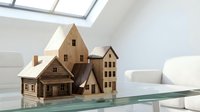 Wooden miniature house models on glass table in bright modern interior with skylight for architectural design and real estate concepts.