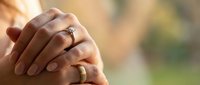 Couple holding hands showing wedding rings in warm sunlight representing love, marriage, commitment and romantic relationship between husband and wife.
