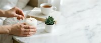 Woman hands holding white ceramic mug with hot beverage on marble table with small succulent plant and tea cup creating cozy morning atmosphere.